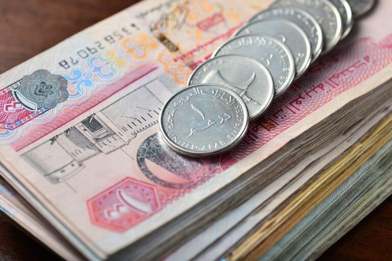 خمس عملات نقدية من فئة واحد درهم اماراتي موضوعة فوق مجموعة من فئات الأموال الورقية الخاصة بالدرهم الاماراتي